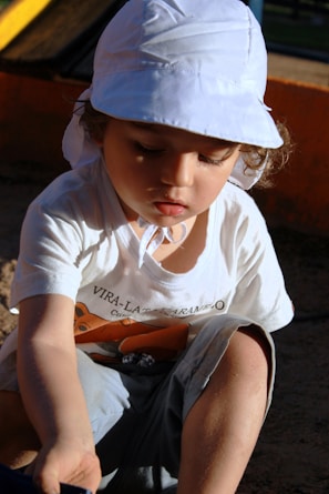 a little girl sitting on the ground wearing a white hat
