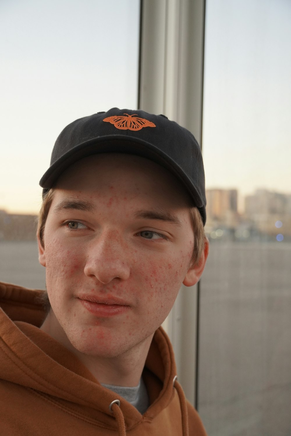 a boy with freckled hair wearing a brown hoodie and a black hat