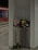 A metal trash bin labeled 'Abfall' is overflowing with various waste items such as paper cups, bottles, and bags. The surroundings appear to be a train or metro station, identifiable by the red train visible in the background. On the ground, near the base of the bin, are scattered flowers, including long-stemmed roses.