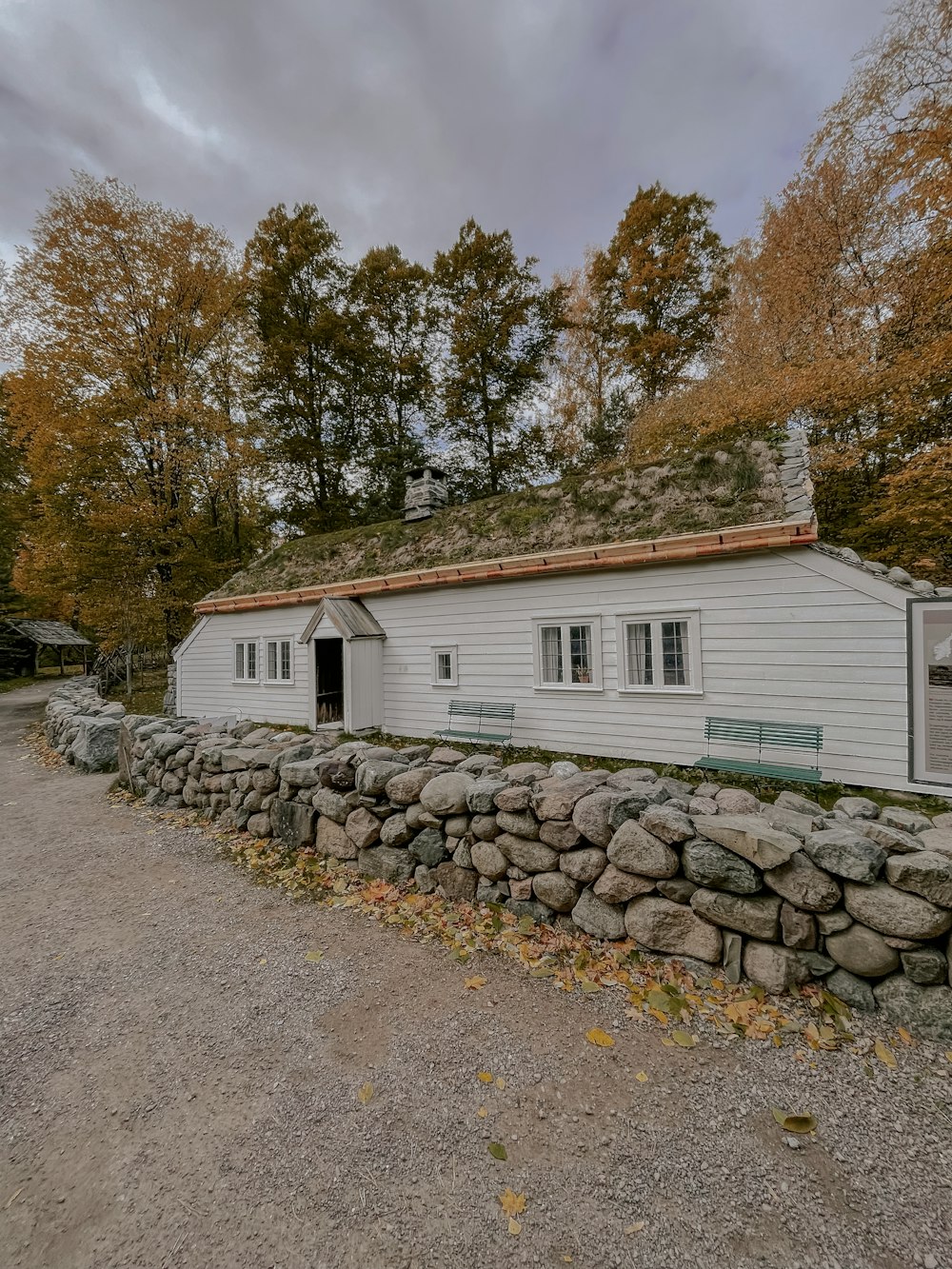 a white house with a stone wall and a green roof