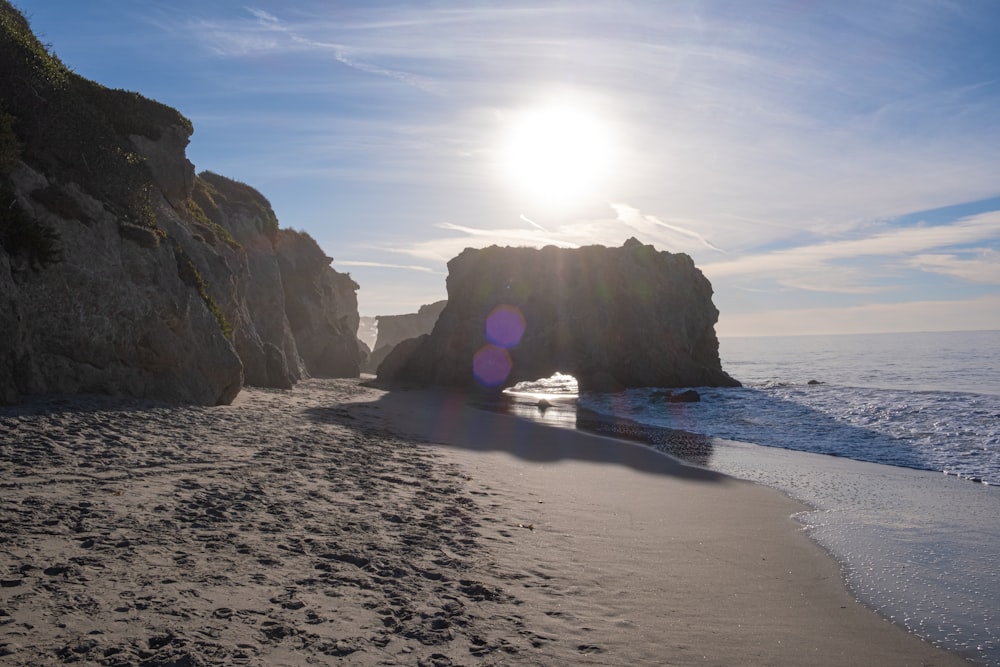 the sun shines brightly on a beach near a rock formation