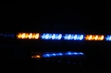 A series of bright, flashing LED lights in blue and amber are positioned in a dark environment, likely indicating an emergency or service vehicle such as a police car or ambulance.