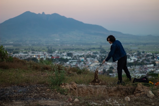 Miner working with a professional metal detector on a green hillside at sunrise.
