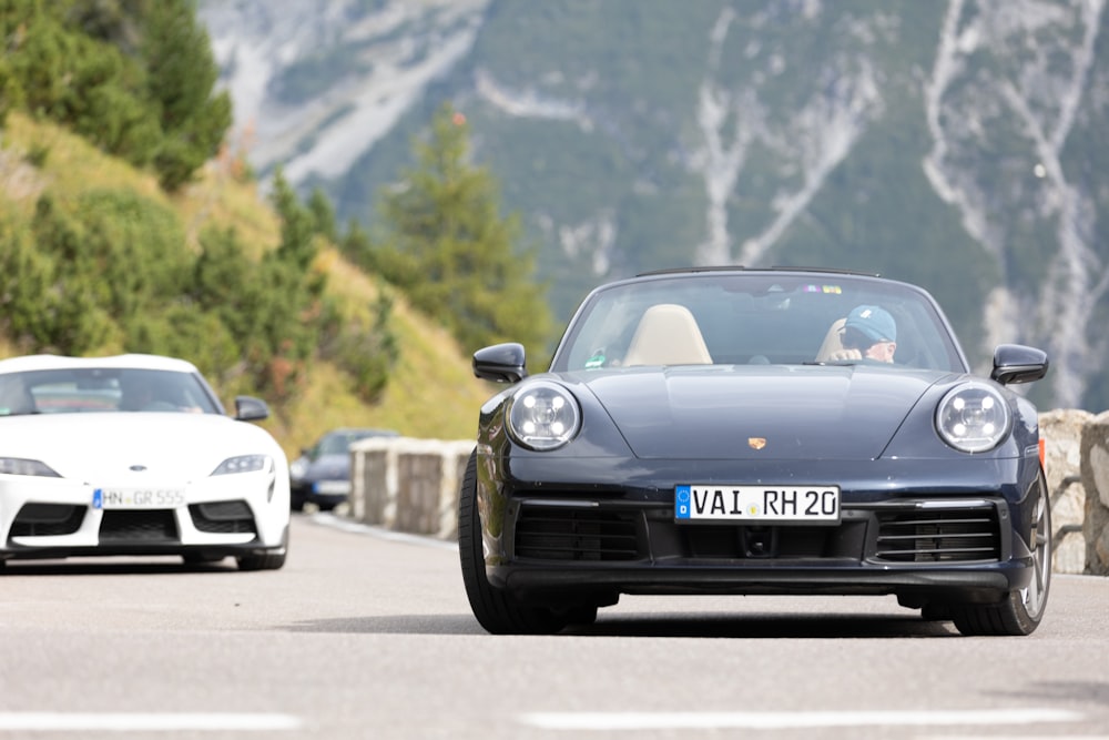 a couple of cars driving down a road next to a mountain