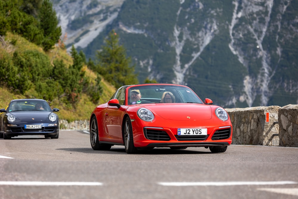 a couple of cars driving down a road next to a mountain