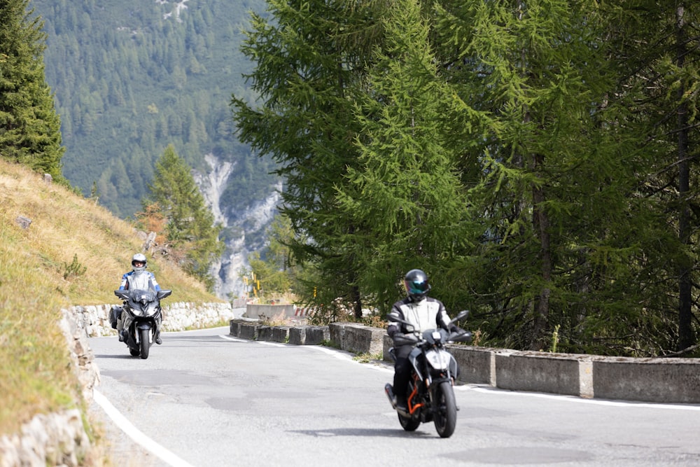 two motorcyclists riding down a road in the mountains