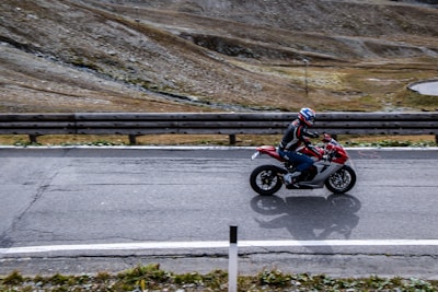 A rider wearing a helmet riding a red motorcycle on a winding road.