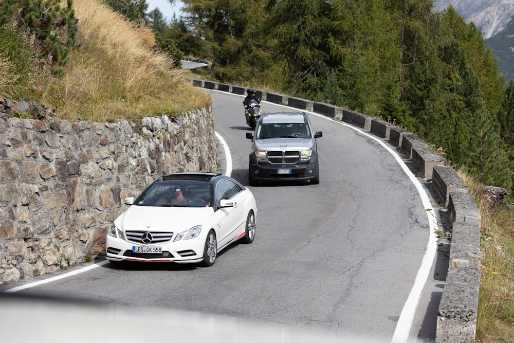 two cars driving down a road next to a stone wall