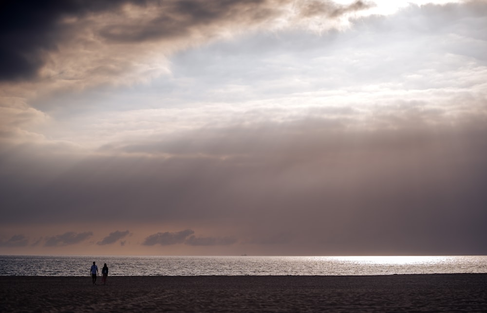 a couple of people standing on top of a sandy beach