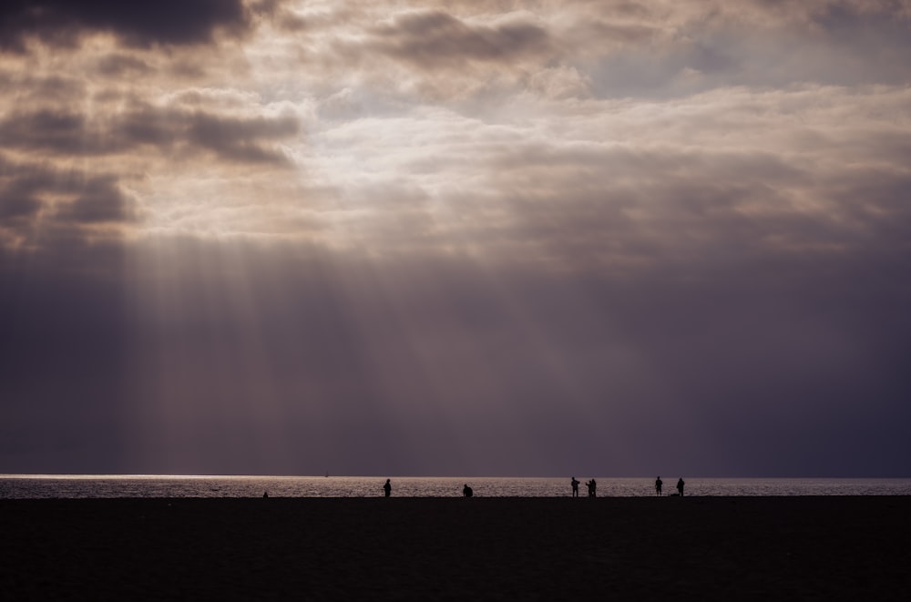 a group of people standing on top of a beach under a cloudy sky