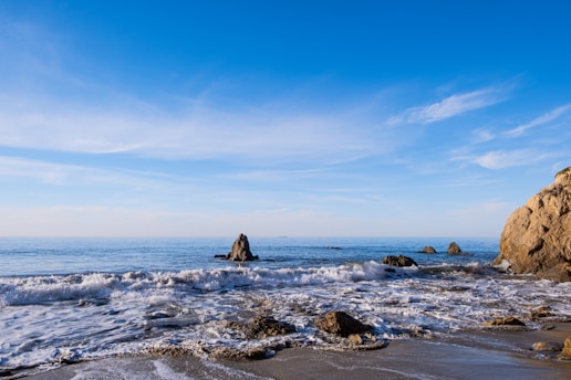 A serene coastal landscape with waves gently rolling onto the shore under a clear blue sky.