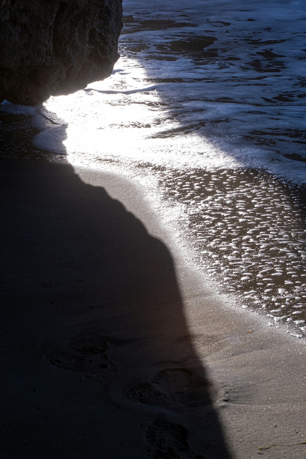 the shadow of a person standing on a beach next to the ocean