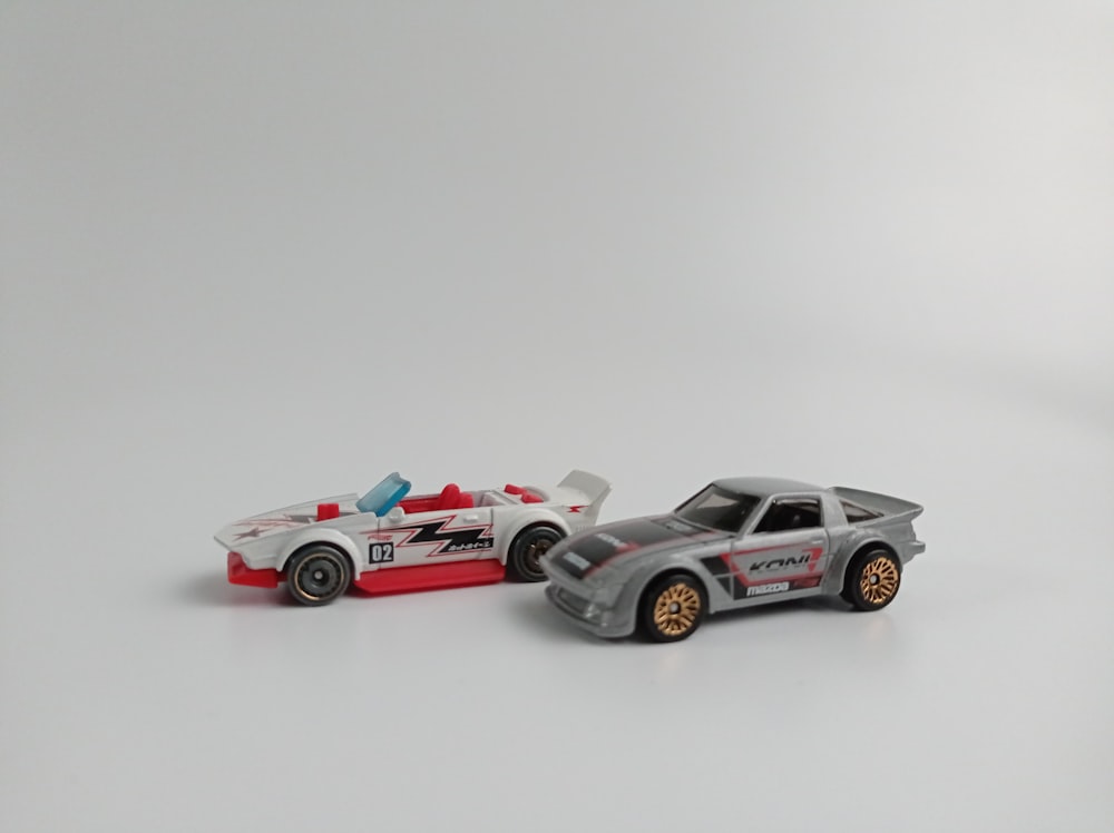 two toy cars sitting side by side on a white surface