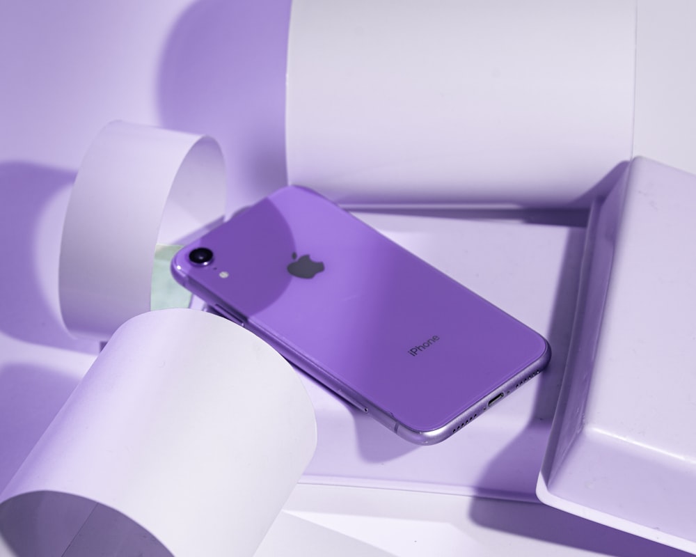 a purple iphone sitting on top of a toilet paper roll