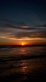 the sun is setting over the ocean on a cloudy day