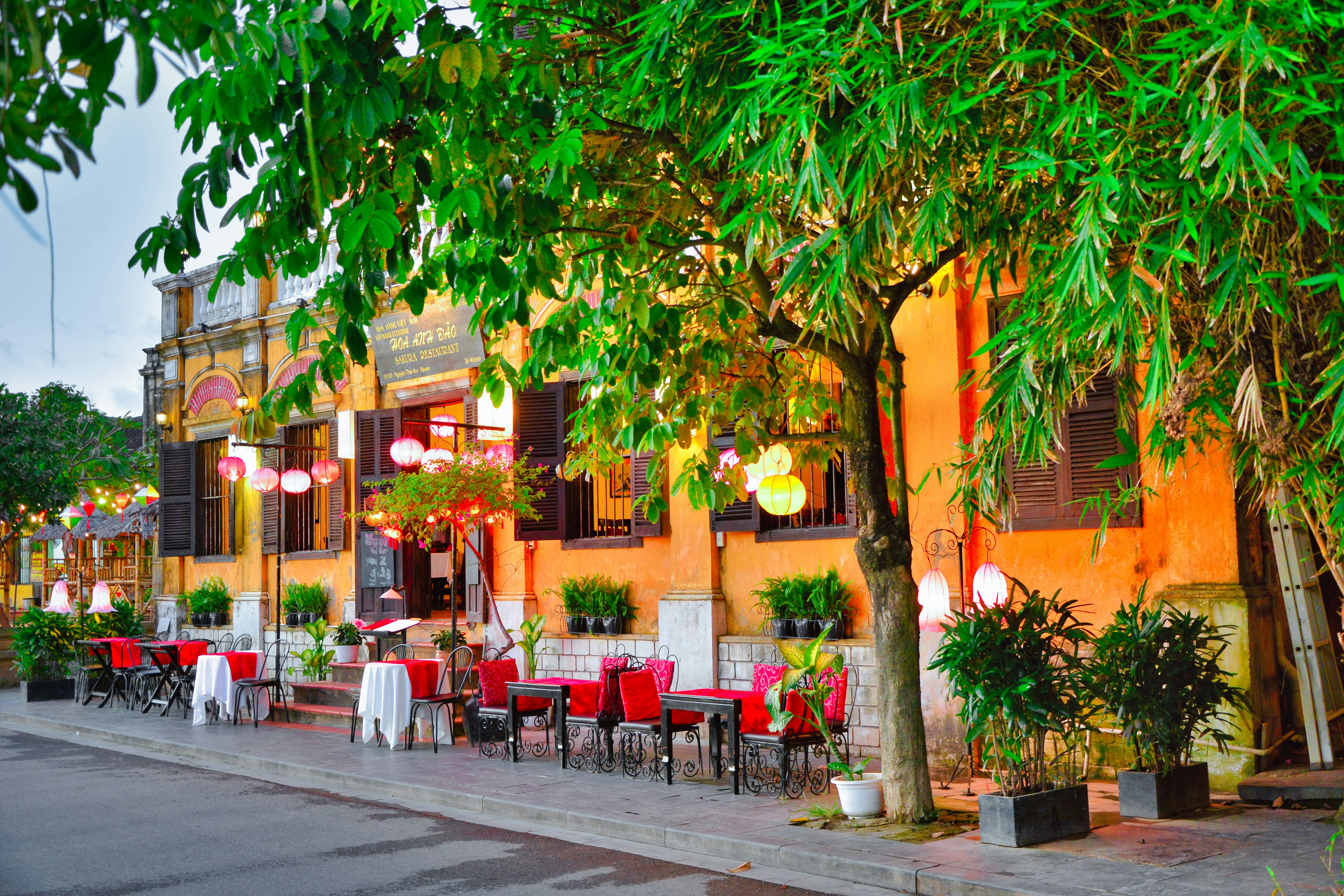 a restaurant with tables and chairs under a tree, ancient colonial city of Hoi An, Vietnam