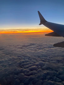A scenic view of an airplane flying over clouds at sunset.