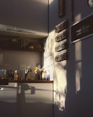 A cozy kitchen corner bathed in warm, late-afternoon sunlight. The wall is decorated with a hexagonal tile backsplash and shelves holding rows of spice jars. A sign reads 'This kitchen is for dancing'. Shadows of nearby objects are cast on the wall, adding artistic flair to the space.