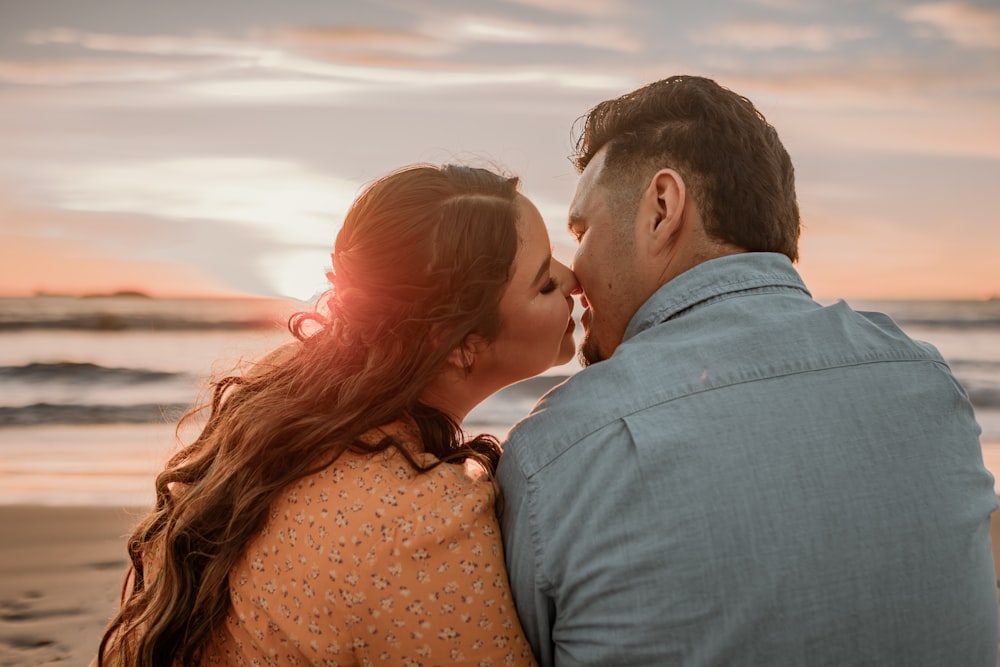 a man and a woman sitting on a beach kissing