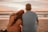 a man and woman sitting on the beach watching the sunset