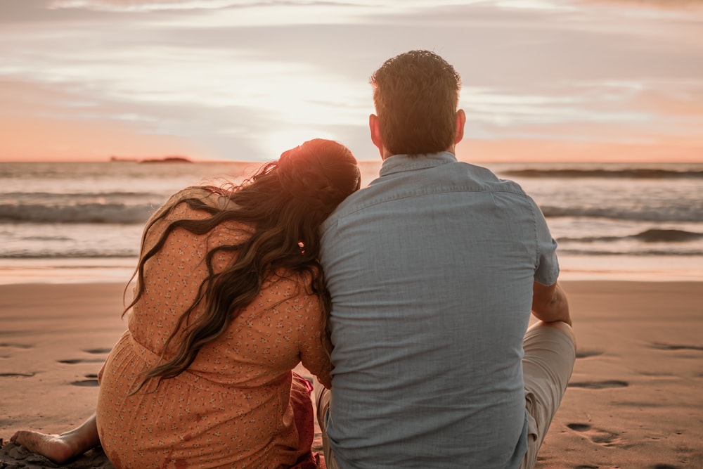 un homme et une femme assis sur la plage regardant le coucher du soleil