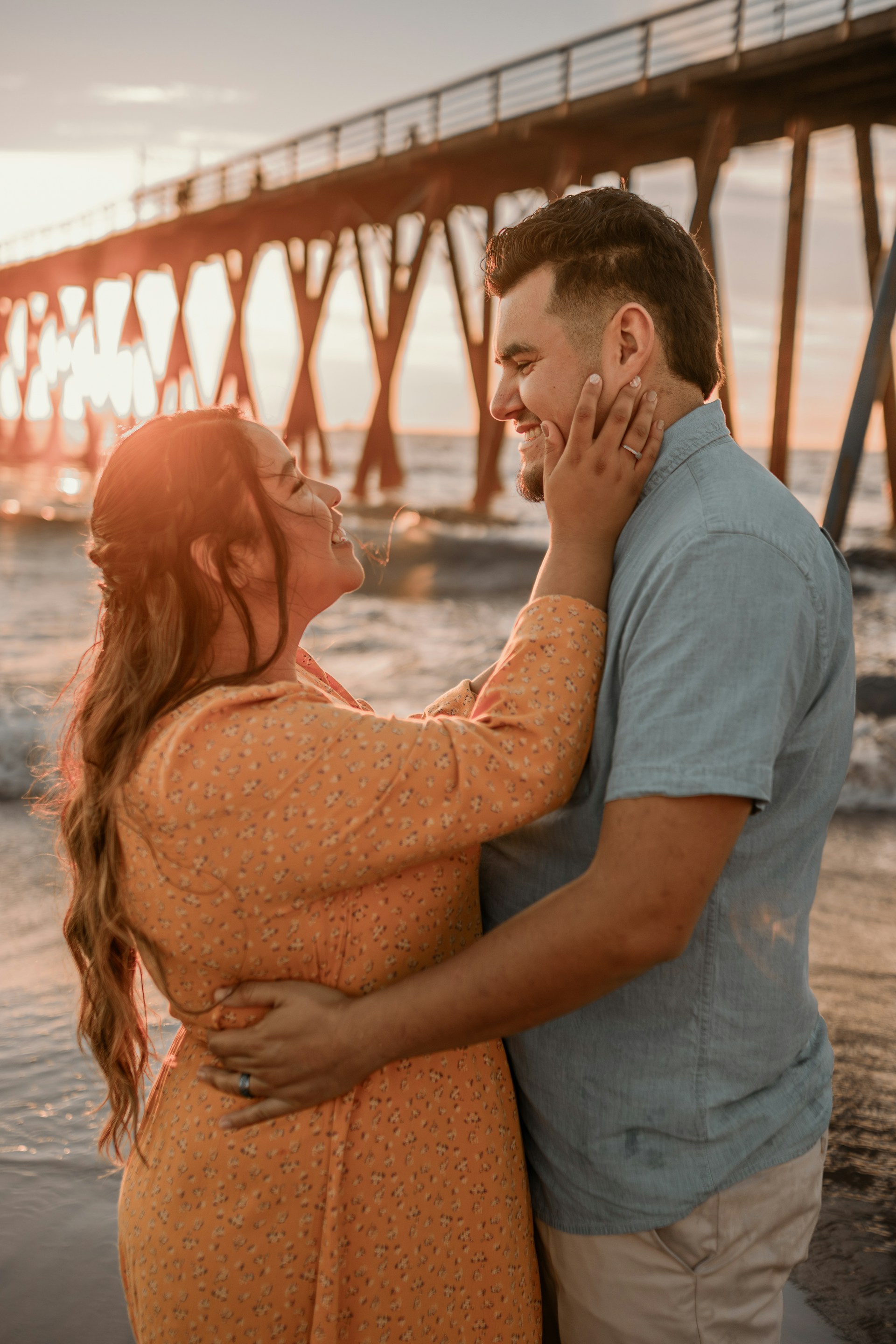 A couple embraces on the shoreline, with gentle waves lapping at their feet and the sun dipping on the horizon.