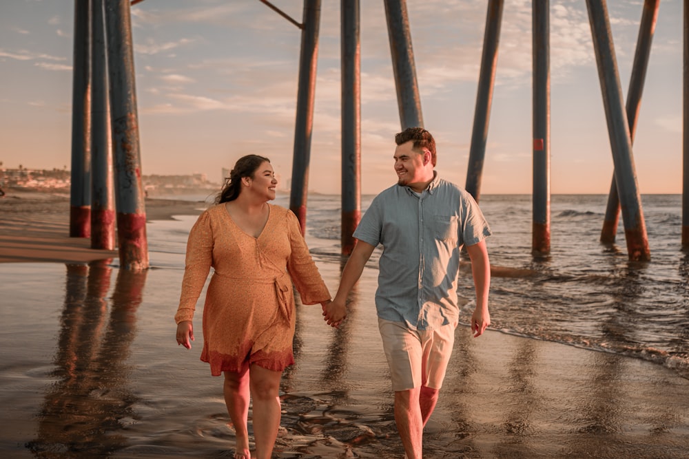 a man and a woman walking on the beach holding hands