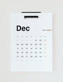 A minimalistic wall calendar for December 2023, with days of the week listed at the top starting from Monday. The calendar is predominantly white with black text and a subtle touch of gold used for Sundays and the number 25, suggesting Christmas.