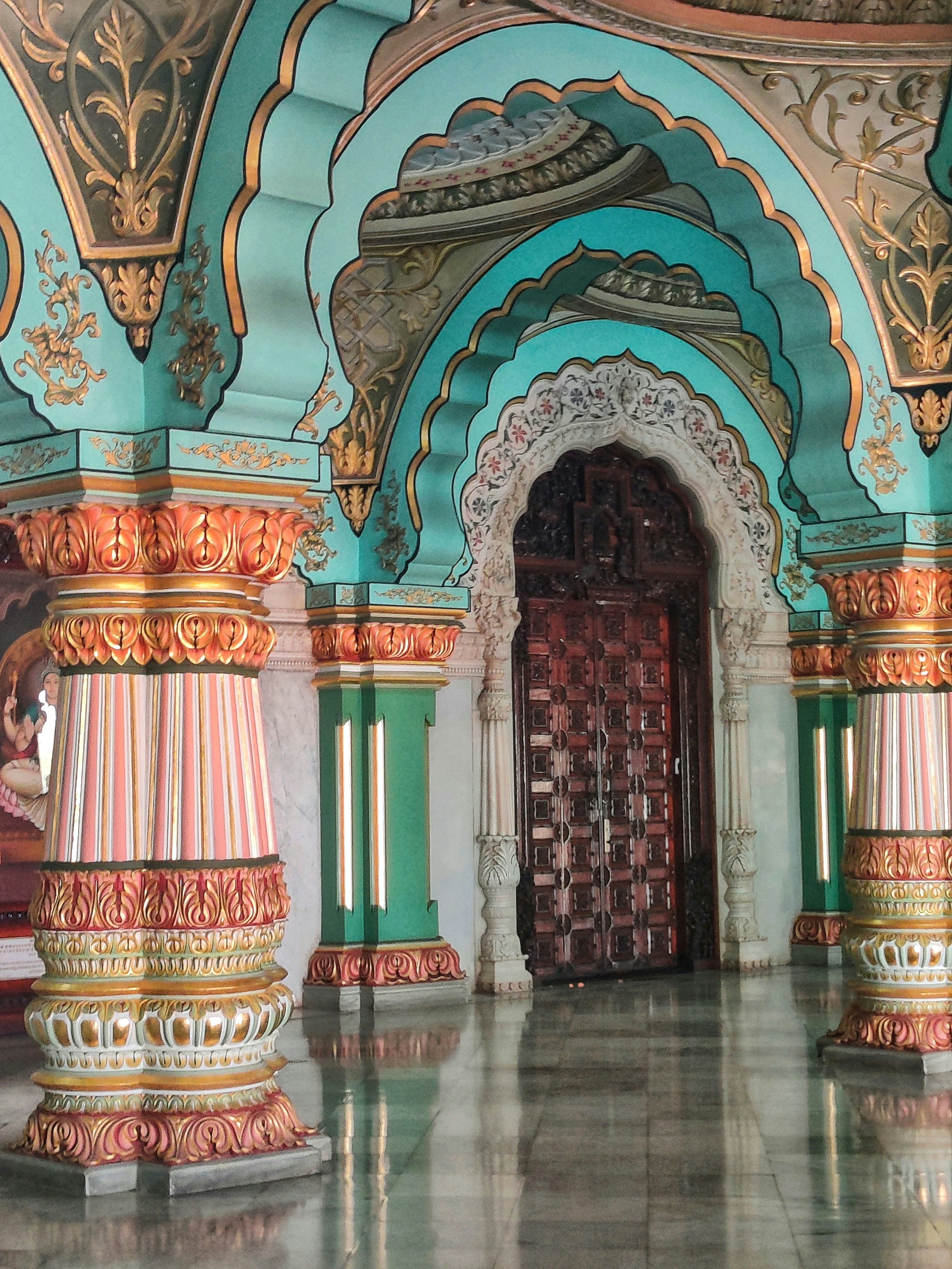 Elegant wooden palace with ornate arched balconies, intricate teak carvings, and floral murals in warm ochre tones
