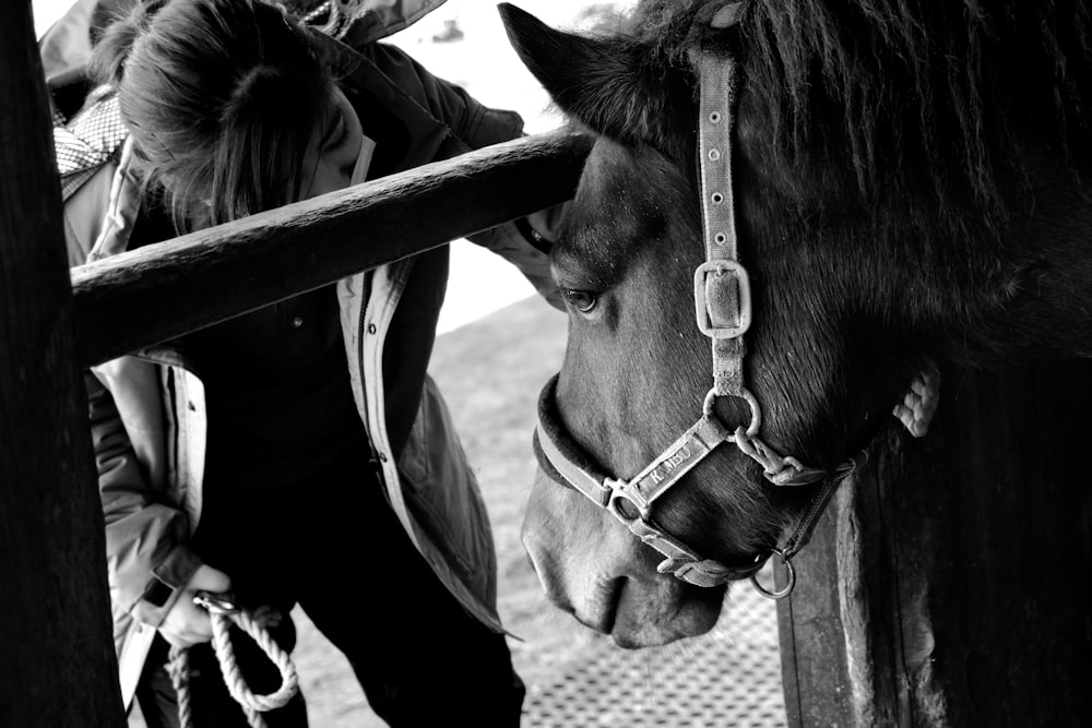 a black and white photo of a woman petting a horse