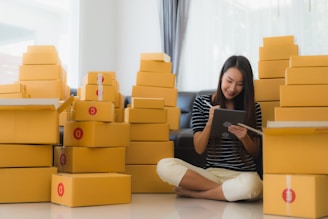 Photo of a woman coordinating logistics on a tablet in an office with moving boxes.