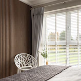 A cozy bedroom corner featuring white and beige linen draped over a chair near a window