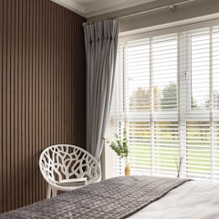 A minimalist bedroom corner featuring a sculptural chair and soft layered textiles.