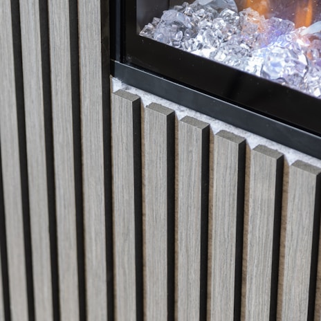 Vertical wooden slats are arranged next to a glass panel containing decorative ice-like crystals. The wood appears to have a natural finish, and the glass panel reflects some light, creating a contrast between the materials.