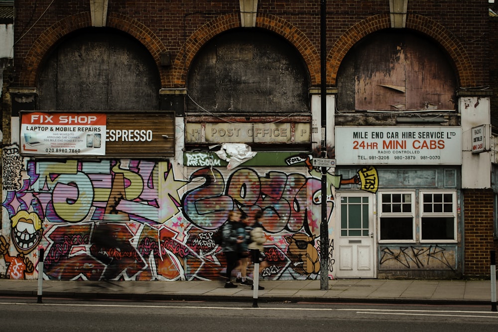 a person sitting on a bench in front of a building covered in graffiti