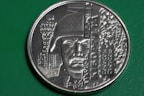 A commemorative coin featuring a detailed relief of a soldier's face wearing a helmet. The design includes intricate details of a building on the left and patterns or inscriptions that appear to be Cyrillic text. The dates 26.05.2014 to 21.01.2015 are visible on the coin's face.