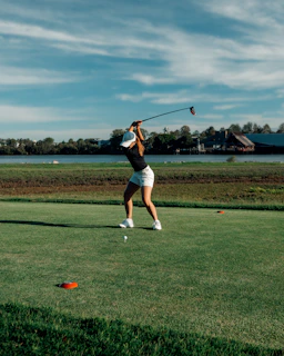 a woman swinging a golf club on top of a green field