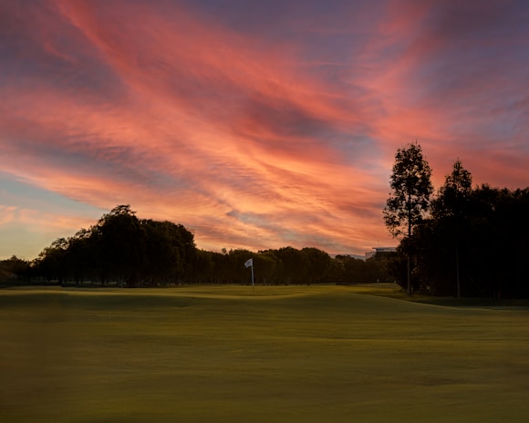 A scenic view of a lush green golf course at sunset.
