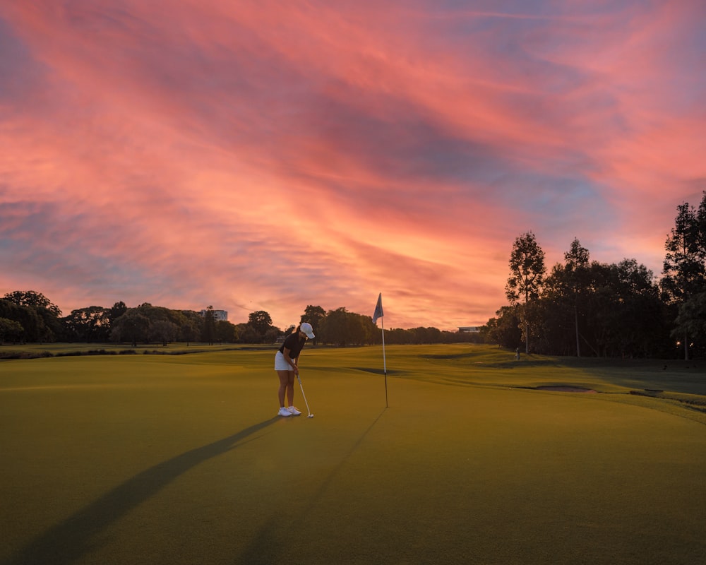 a woman standing on top of a green holding a golf club