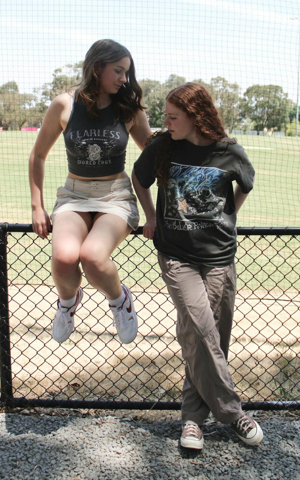 two young women standing next to each other near a fence