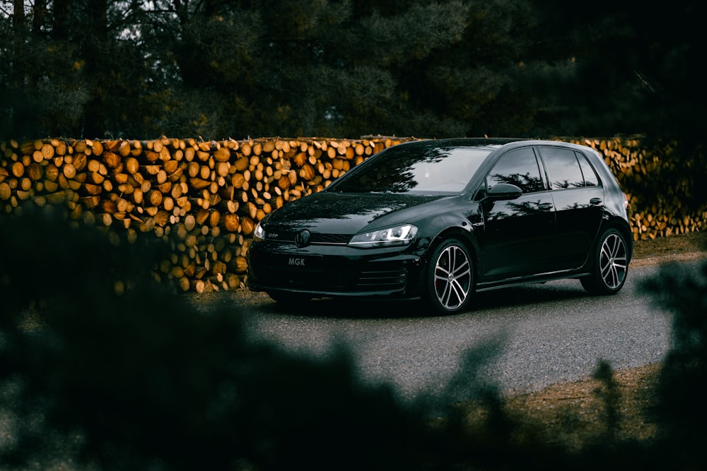 a black car parked next to a pile of logs