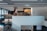 A large, modern indoor space featuring a multi-level bookstore or library. Books and magazines are neatly arranged on shelves, and a person is sitting at a table working on a laptop. The design is sleek, with clean lines and contemporary lighting.