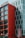 A modern hotel building with a striking facade featuring large red panels and a contrasting gray section with vertical window arrangements. The signage at the top indicates it is a hotel, while street signs are visible at ground level.