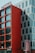 A modern hotel building with a striking facade featuring large red panels and a contrasting gray section with vertical window arrangements. The signage at the top indicates it is a hotel, while street signs are visible at ground level.