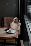 A stylish tote bag hanging on a café chair with a coffee cup and notebook nearby.