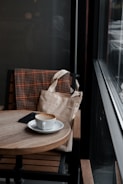 A stylish tote bag hanging on a café chair with a coffee cup and notebook nearby.