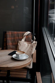 A cozy scene showing a shoulder bag casually placed next to a coffee cup on a café table.