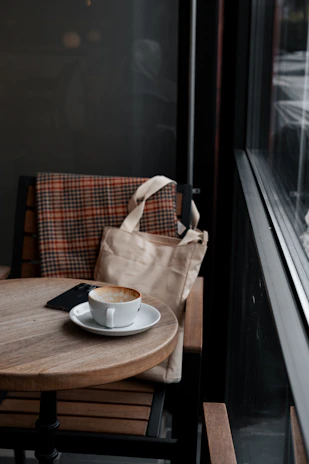 A stylish leather-trimmed tote bag resting on a wooden bench in a cozy café.