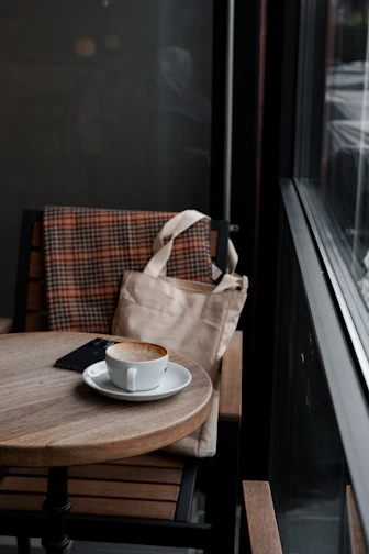 A stylish leather-trimmed tote bag resting on a wooden bench in a cozy café.