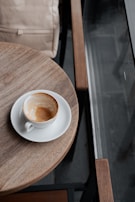 A backpack resting next to a steaming cup of coffee on a train table during a rainy day trip.
